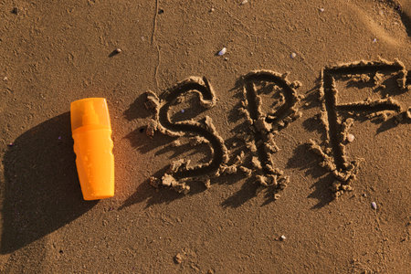 Creative composition with bottle of sunscreen cream on sand at sea beach