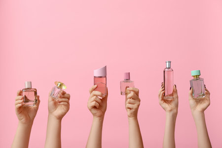 Female hands holding different perfumes on pink backgroundの写真素材