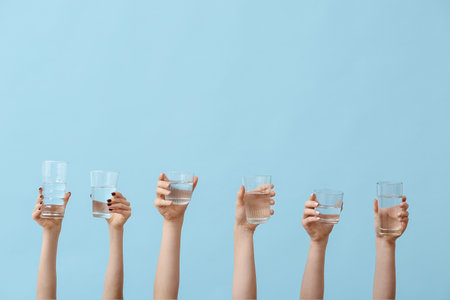 Female hands holding glasses of water on blue backgroundの写真素材