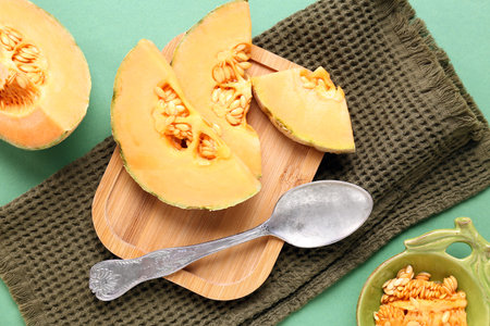Wooden board with pieces of sweet melon on green background
