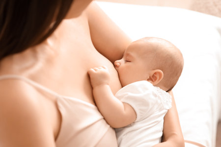 Young woman breastfeeding her baby in bedroom, closeupの写真素材