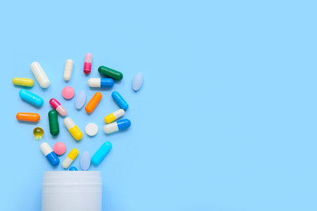 Overturned bottle with different pills on color background