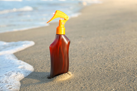 Bottle of sunscreen cream on sand near ocean at beachの写真素材