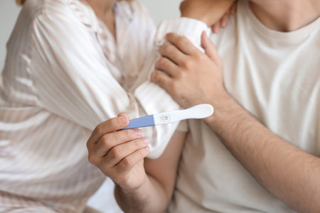 Happy young couple with pregnancy test in bedroom, closeup