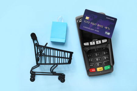 Small shopping cart with bags, payment terminal and credit card on blue background