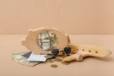 Wooden piggy bank with money, toy airplane and passport on beige background. Concept of savings for travelの写真素材