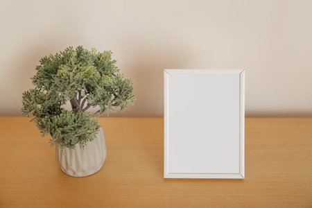 Blank frame and decorative tree in pot on wooden table, closeup