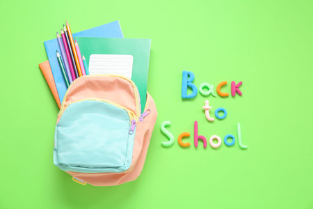 Text BACK TO SCHOOL, backpack and stationery on green background