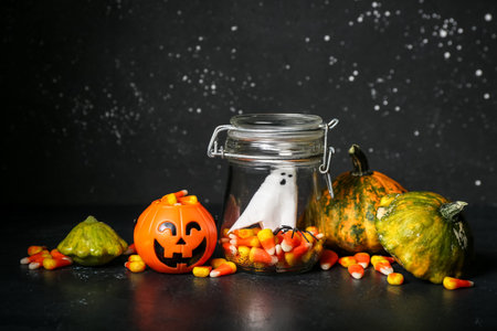 Glass jar with tasty candy corns and squashes on dark background. halloween celebration concept