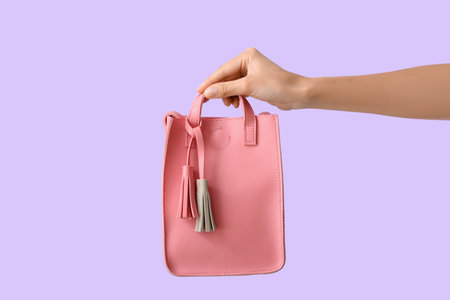 Female hand with stylish pink handbag on lilac backgroundの写真素材