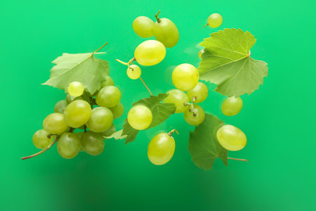 Flying sweet green grapes with leaves on color background