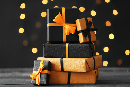 Gift boxes for Halloween celebration on black wooden table against blurred lights