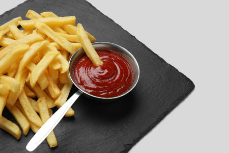 Black slate board with golden french fries and ketchup on gray background, closeupの写真素材