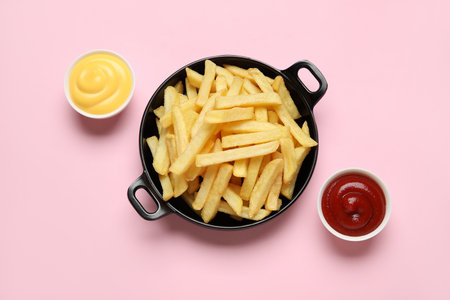 Black bowl with golden french fries, ketchup and cheese sauce on pink backgroundの写真素材
