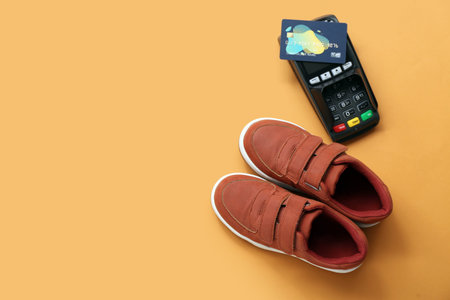 Pair of stylish child's shoes, payment terminal and credit card on color backgroundの写真素材