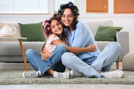 Little girl and her mother with hair curlers hugging at homeの写真素材