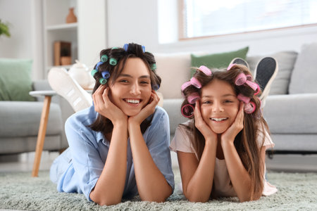 Little girl with her mother curling hair at homeの写真素材