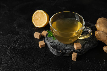 Glass cup of ginger tea with lemon and mint on black backgroundの写真素材
