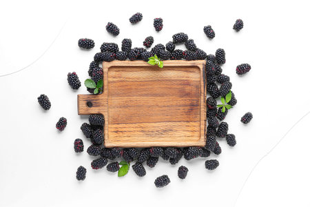 Wooden board with fresh blackberries and leaves on white background