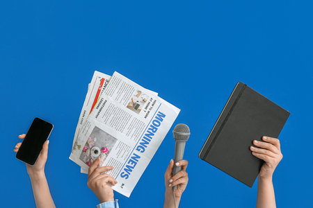 Female hands with mobile phone, newspapers, microphone and notebook on blue backgroundの写真素材