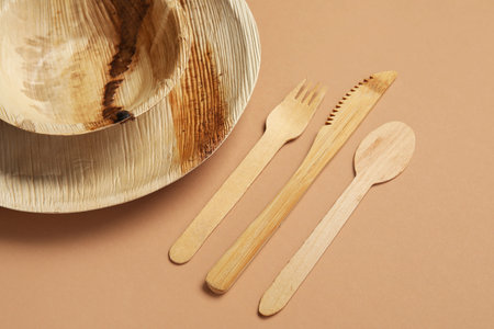 Wooden cutlery with plate and bowl on brown background, closeup