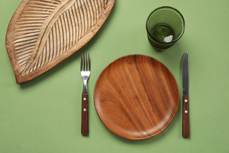 Wooden plate, board, cutlery and glass on green backgroundの写真素材
