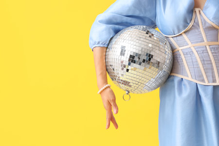 Fashionable young woman with disco ball on yellow backgroundの写真素材