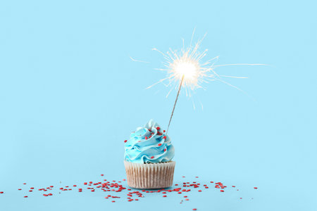 Tasty birthday cupcake with sparkler on blue backgroundの写真素材