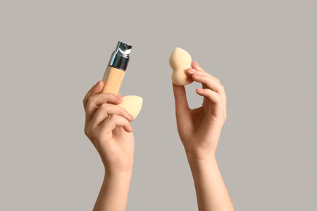 Female hands with makeup sponges and bottle of foundation on gray backgroundの写真素材