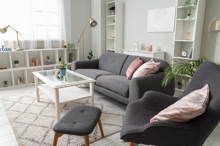 Interior of light living room with gray armchair, footstool and sofa