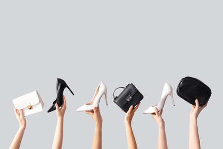 Female hands holding different stylish bags and high heels on gray backgroundの写真素材