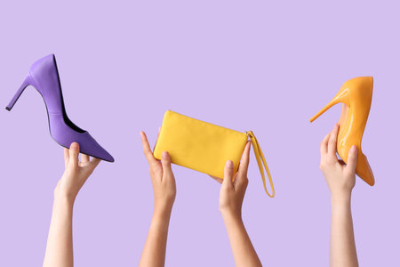 Female hands holding different stylish bags and high heels on lilac backgroundの写真素材