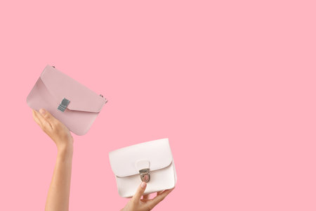 Female hands holding stylish women's bags on pink backgroundの写真素材