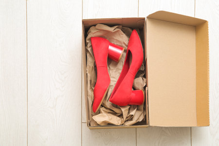 Cardboard box with stylish high heeled shoes on floorの写真素材