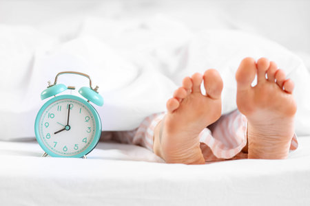 Sleeping woman's feet with alarm clock in bed, closeupの写真素材