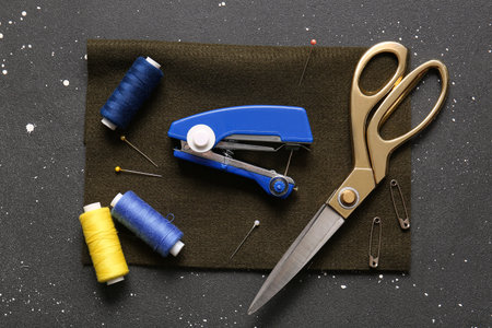 Manual sewing machine with different supplies on grunge black background