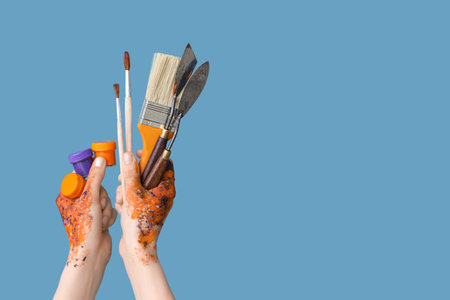 Female hands with paintbrushes, gouache and palette knives on blue backgroundの写真素材