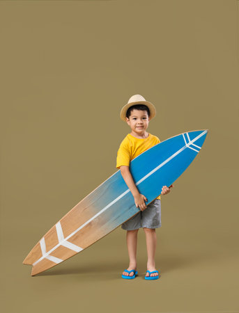 Cute little Asian boy with surfboard on green background