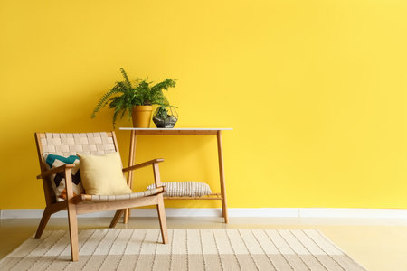 Stylish armchair and houseplant on console table near yellow wallの写真素材