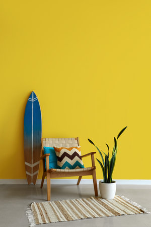 Stylish armchair, surfing board and houseplant near yellow wallの写真素材