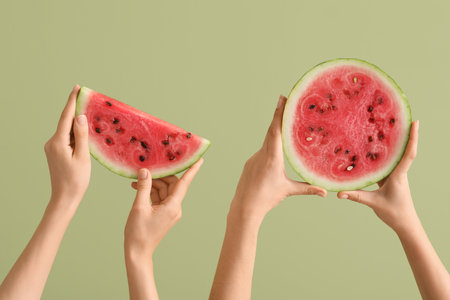 Female hands with half and slice of ripe watermelon on green backgroundの写真素材