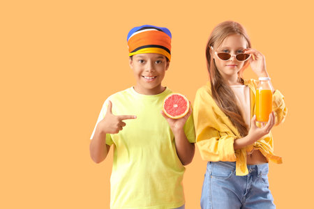 Little children with bottle of fresh citrus juice and grapefruit slice on orange backgroundの写真素材