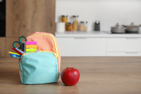 Stylish school backpack with stationery and fresh apple on table in kitchenの写真素材