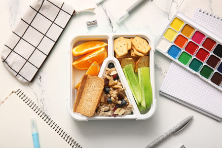Lunchbox with delicious food and different stationery on grunge white background