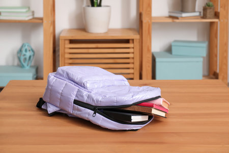 Stylish school backpack with books on wooden table in living room
