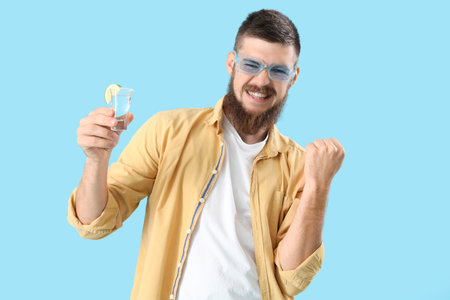Cheerful young man with shot of tequila on blue backgroundの写真素材