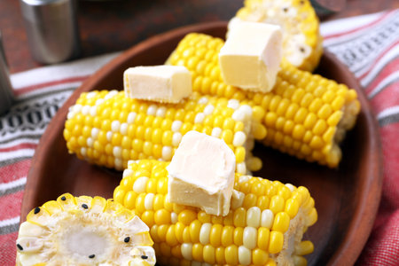 Plate of boiled corn cobs with butter on dark background