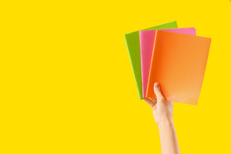 Hand with notebooks on yellow background