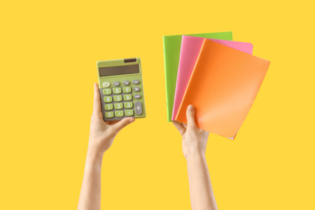 Hands with notebooks and calculator on yellow backgroundの写真素材