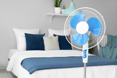 Floor fan and cozy bed in interior of light bedroomの写真素材